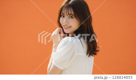 自然な笑顔のオレンジ背景での若い女性ポートレート 128814055