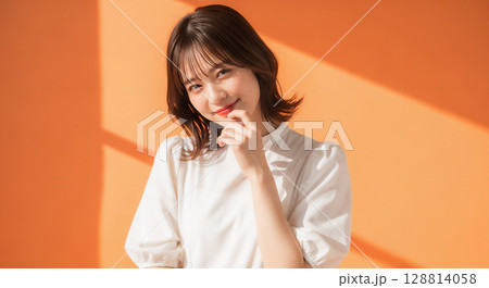 自然な笑顔のオレンジ背景での若い女性ポートレート 128814058