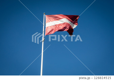 Latvian National Flag Fluttering in the Wind Against a Bright Blue Sky Background Latvian National Flag Fluttering in the Wind Against a Bright Blue Sky Background 128814515