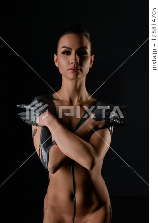 Confident woman poses creatively with striking body art in dark setting 128814705