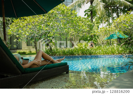Woman relaxes by the peaceful pool in lush greenery 128816200