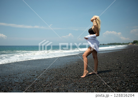Woman stands on black sand beach enjoying the warm sun 128816204