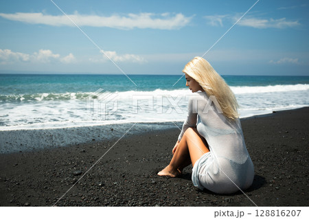 Woman on sandy shore gazing at waves and skyline 128816207