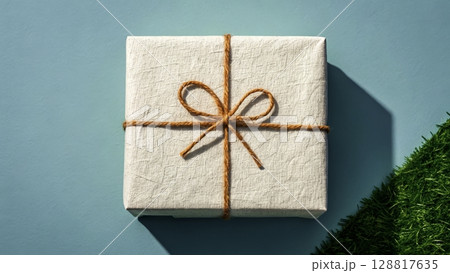 Gift box elegantly wrapped with twine and set against a bright blue background with green grass 128817635