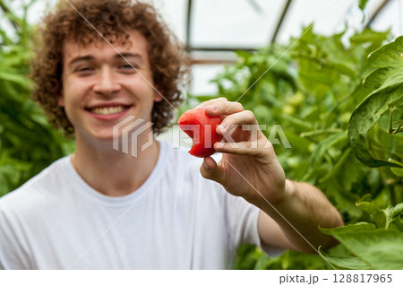 Happy young man showing bitten tomato in greenhouse 128817965