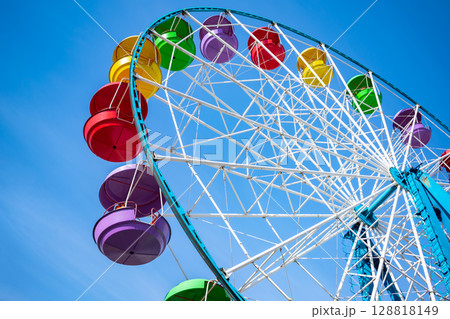 Ferris wheel with colorful cabins against a clear sky Ferris wheel with colorful cabins against a clear sky 128818149