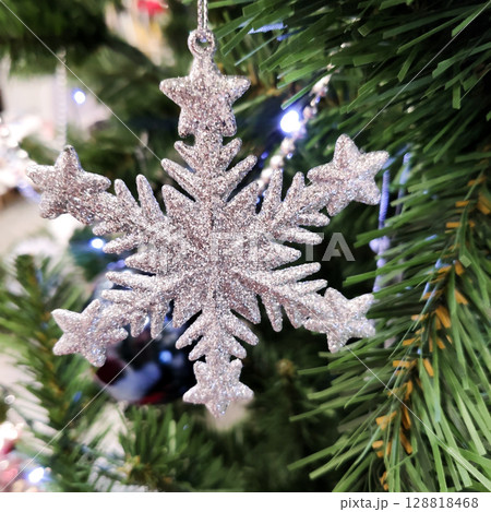 Close-up of a white artificial snowflake with glitter on a Christmas tree branch. Festive photo of Christmas decor. 128818468
