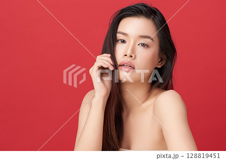 A beautiful young Asian woman with clean, fresh skin against a red background. Skincare, facial treatment, cosmetology, beauty, and spa. An elegant portrait of an Asian woman. A beautiful young Asian woman with clean, fresh skin against a red background. Skincare, facial treatment, cosmetology, beauty, and spa. An elegant portrait of an Asian woman. 128819451