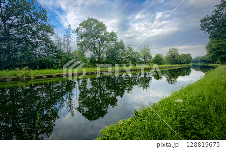 A picturesque and scenic riverside reflection showcasing lush greenery beneath a cloudy sky 128819673