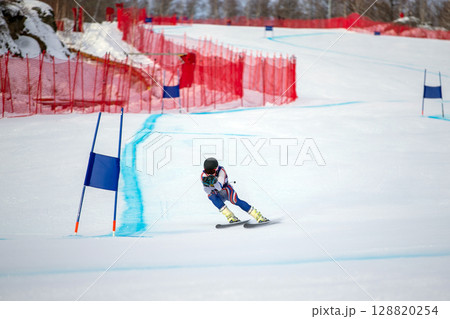 alpine skier racing downhill on snowy ski slope during giant slalom competition alpine skier racing downhill on snowy ski slope during giant slalom competition 128820254