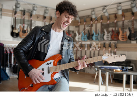 A man in a leather jacket is playing guitar in a store A man in a leather jacket is playing guitar in a store 128821567