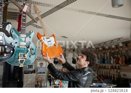 Musician intently exploring various electric guitars in a vibrant music store Musician intently exploring various electric guitars in a vibrant music store 128821618