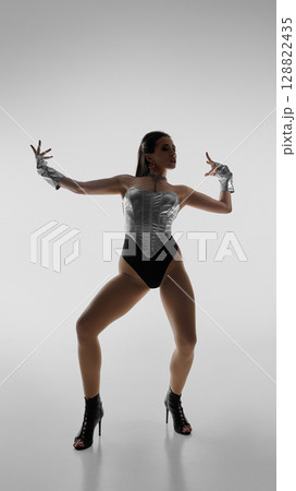 Elegant dancer striking dynamic pose in high heels against plain background 128822435