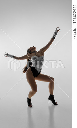 Dancer in silver leotard striking dynamic pose in high heels against white background Dancer in silver leotard striking dynamic pose in high heels against white background 128822436