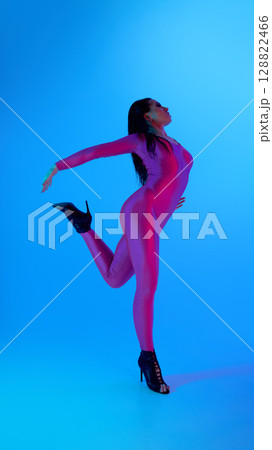 Dancer in vibrant jumpsuit posing elegantly against blue background Dancer in vibrant jumpsuit posing elegantly against blue background 128822466