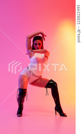 Dancer striking a pose in high heels against a colorful pink and orange backdrop 128822495