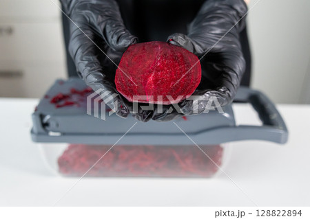 Hands in black protective gloves hold a vibrant red beetroot half over a kitchen grater, demonstrating healthy food preparation and kitchen safety Hands in black protective gloves hold a vibrant red beetroot half over a kitchen grater, demonstrating healthy food preparation and kitchen safety 128822894