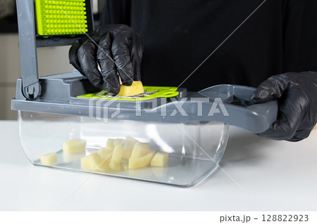 A person wearing black gloves actively uses a multi-functional kitchen vegetable chopper, dicing fresh potatoes, illustrating efficient home food preparation for nutritious meals easily 128822923