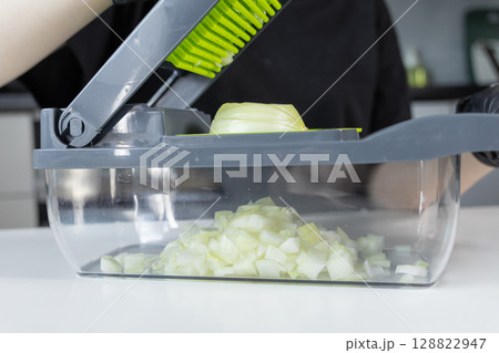 A person utilizes an innovative kitchen vegetable chopper to quickly dice a fresh onion, illustrating efficient food preparation for healthy home cooking and convenience A person utilizes an innovative kitchen vegetable chopper to quickly dice a fresh onion, illustrating efficient food preparation for healthy home cooking and convenience 128822947