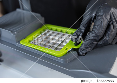 Person using a sharp grid blade insert for a modern kitchen vegetable chopper, emphasizing efficient food preparation and professional cooking convenience 128822953