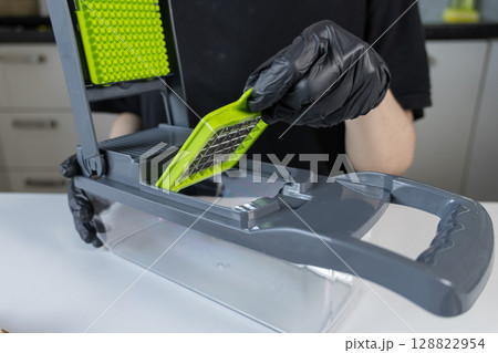 Person in black gloves meticulously assembling a multi-functional modern kitchen vegetable chopper, inserting a sharp green blade for efficient food preparation Person in black gloves meticulously assembling a multi-functional modern kitchen vegetable chopper, inserting a sharp green blade for efficient food preparation 128822954