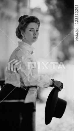 Black and white portrait of woman with vintage hairstyle holding hat and looking distant Black and white portrait of woman with vintage hairstyle holding hat and looking distant 128823292