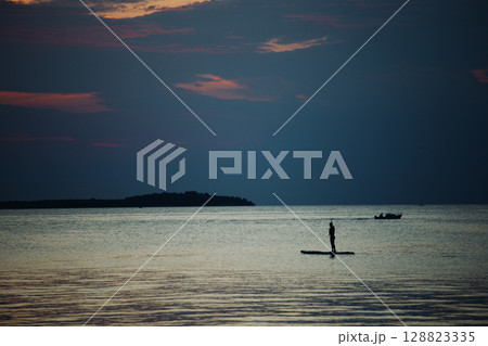 A swimmer stands on a sup board in the middle of the sea on a summer evening at A swimmer stands on a sup board in the middle of the sea on a summer evening at 128823335