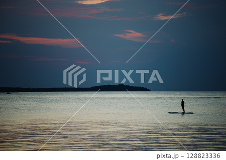 A swimmer stands on a sup board in the middle of the sea on a summer evening at A swimmer stands on a sup board in the middle of the sea on a summer evening at 128823336