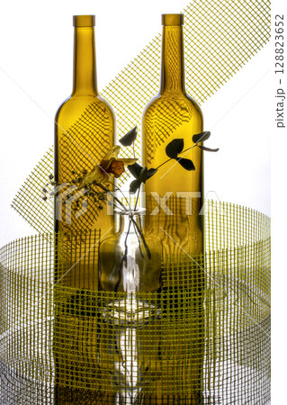 Still life with glass bottles, flowers and yellow mesh on a white background Still life with glass bottles, flowers and yellow mesh on a white background 128823652
