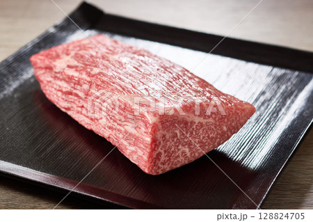 A5ランク黒毛和牛のもも肉ブロックを黒い角皿に盛り付けた高級感あふれる食材写真 128824705