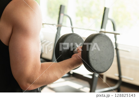 Close up of muscular arm lifting dumbbell in gym setting. Weightlifting exercises, physical fitness. Work out. Close up Close up of muscular arm lifting dumbbell in gym setting. Weightlifting exercises, physical fitness. Work out. Close up 128825143
