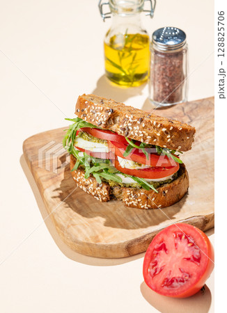 Sandwich of grain bread with tomatoes, mozzarella, arugula and pesto on a wooden board Sandwich of grain bread with tomatoes, mozzarella, arugula and pesto on a wooden board 128825706
