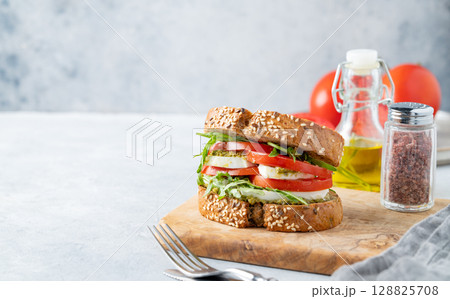 Sandwich of grain bread with tomatoes, mozzarella, arugula and pesto on a wooden board  128825708