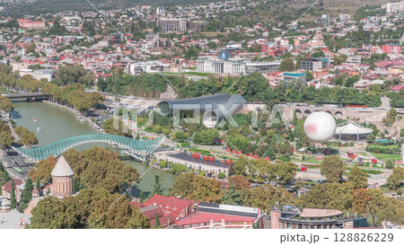 Aerial timelapse of Rike Park, a modern urban park in Tbilisi's Old Town with green trees and lawns. The Bridge of Peace in the background. Georgia 128826229