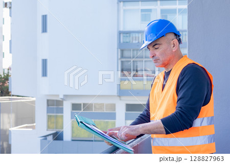 Absorbed construction engineer or building contractor wearing a blue protective helmet checking office blueprints. Copy space Absorbed construction engineer or building contractor wearing a blue protective helmet checking office blueprints. Copy space 128827963