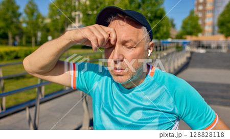 Tired older man wiping sweat during summer outdoor workout Tired older man wiping sweat during summer outdoor workout 128828118