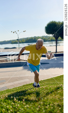Older man in yellow shirt running uphill in city park 128828126