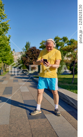 Smiling senior man using smartphone while wearing headphones during outdoor walk 128828130