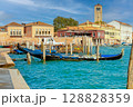 Traditional Venetian waterfront scene on Murano island with gondolas, colorful buildings, and a historic bell tower under sunny skies. 128828359
