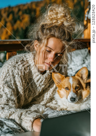 Cozy autumn morning with woman in knitted sweater and her corgi dog, enjoying time together outdoors 128828420