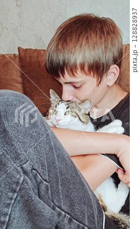 Teenage boy and a cat. Handsome guy hugs his cat while sitting on the couch. Vertical Teenage boy and a cat. Handsome guy hugs his cat while sitting on the couch. Vertical 128828937