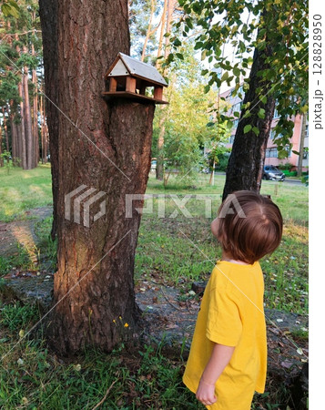 Wooden bird feeder and sparrow Bird feeder, wooden bird house, feeding for birds. child has his back to camera 128828950
