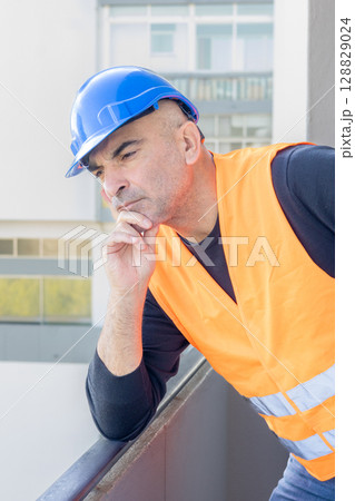 Portrait of an engineer wearing protective workwear posing looking at an unspecified point leaning chin on hand 128829024