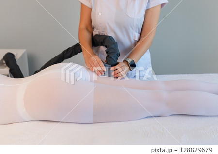 Woman in special white suit getting anti cellulite massage in a spa salon. LPG, and body contouring treatment in clinic.Reset body weight with LPG massage. Woman in special white suit getting anti cellulite massage in a spa salon. LPG, and body contouring treatment in clinic.Reset body weight with LPG massage. 128829679