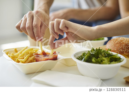 Close-up of two hands dipping french fries into container of ketchup 128830511