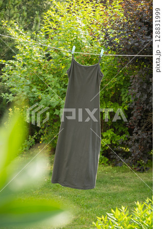 Gray sleeveless shirt hanging on clothesline with clothespins in outdoor garden. Natural environment creates serene and refreshing atmosphere for air drying. 128831999