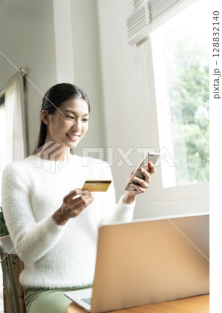 Young Asian woman enjoying a peaceful moment reading a book near window. Calm lifestyle, self-learning, and mindfulness at home. Young Asian woman enjoying a peaceful moment reading a book near window. Calm lifestyle, self-learning, and mindfulness at home. 128832140