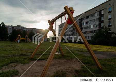 Empty swing set stands on playground in front of apartment building at sunset Empty swing set stands on playground in front of apartment building at sunset 128834994