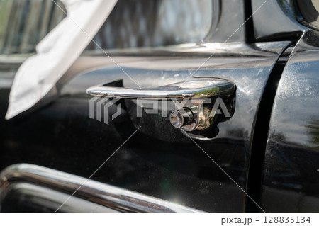 Shiny chrome door handle of classic black car reflecting sunlight 128835134