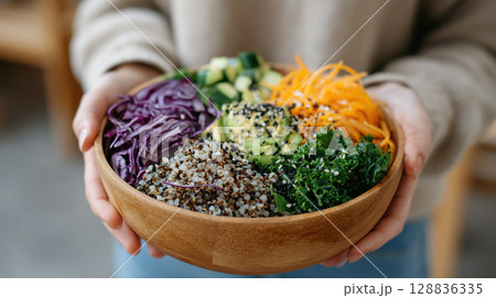 Vibrant bowl of plant based cuisine featuring quinoa, kale, avocado, shredded carrots, and purple cabbage, garnished with sesame seeds 128836335